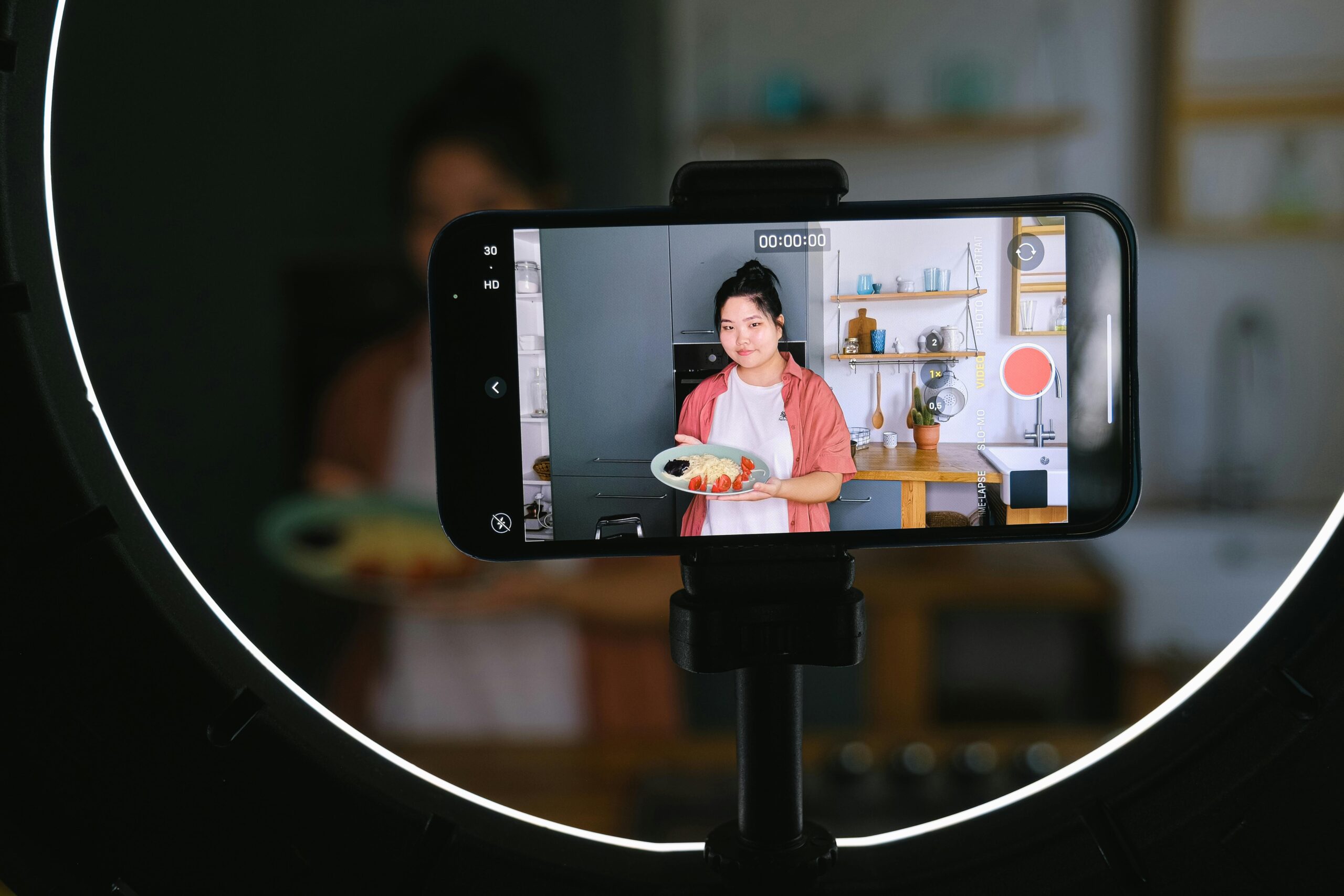 Asian woman recording a cooking tutorial with a smartphone and ring light.